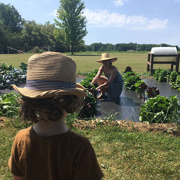 Woman plants in field. Small boy watches