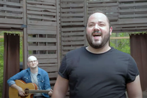 Man seated playing guitar and man standing singing perform in High Park Amphitheatre