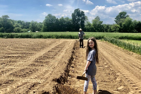 child stands in farmers field with hoe