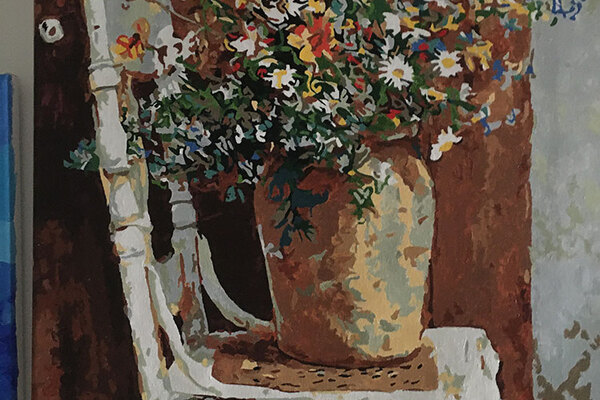 Side view of paint by numbers. White chair with cane seat and vase full of flowers.